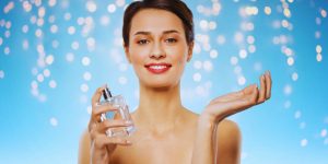 Mulher com um frasco de perfuma na mão esquerda sorrindo para a câmera
