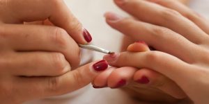 Um parte de mãos femininas segura e passa esmalte na mão de outra mulher
