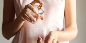 Uma mulher branca de vestido rosa espirrando perfume no próprio pulso