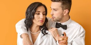 Casal abraçado; nas mãos da mulher, um frasco de perfume